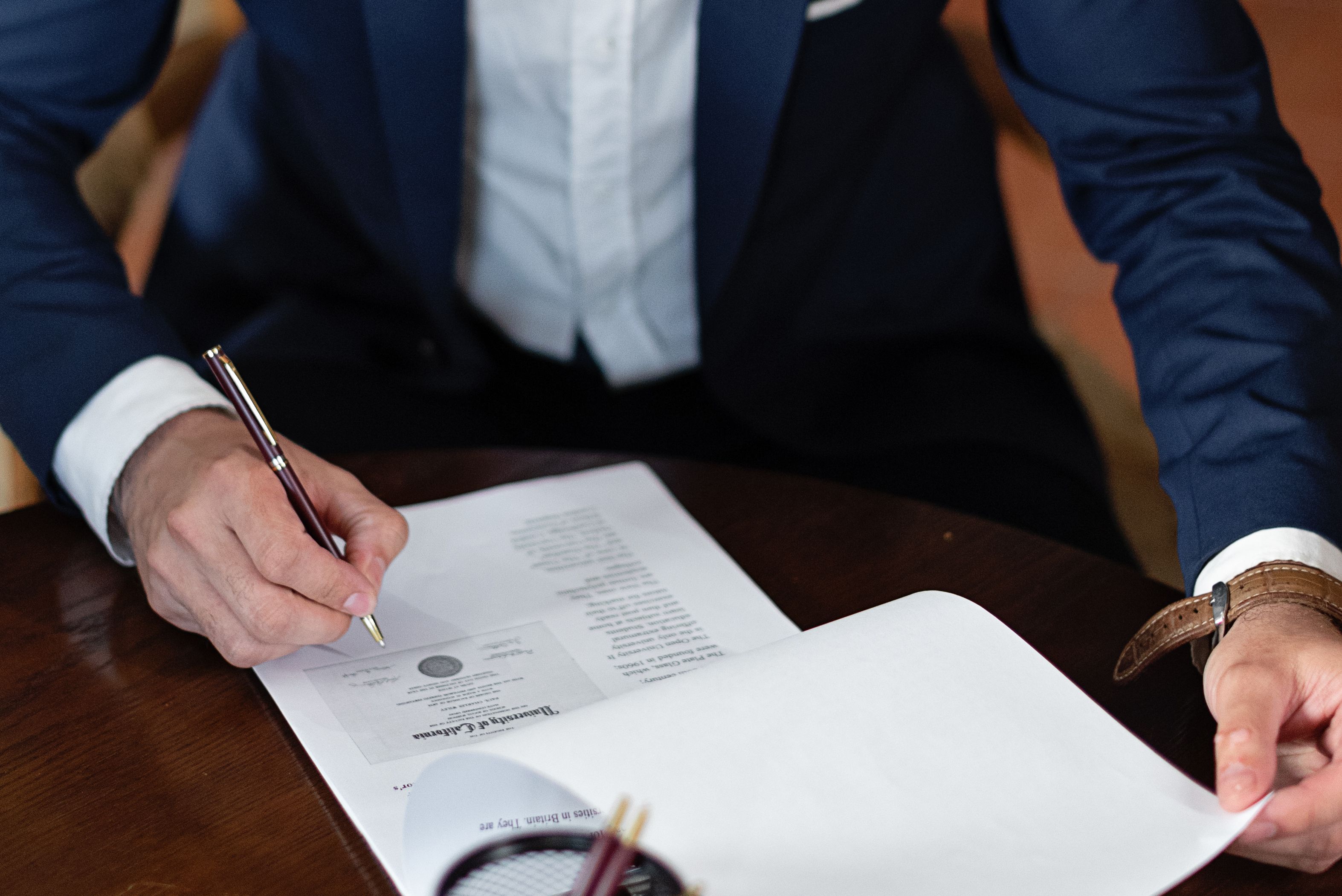 Close de um homem assinando um documento sobre uma mesa